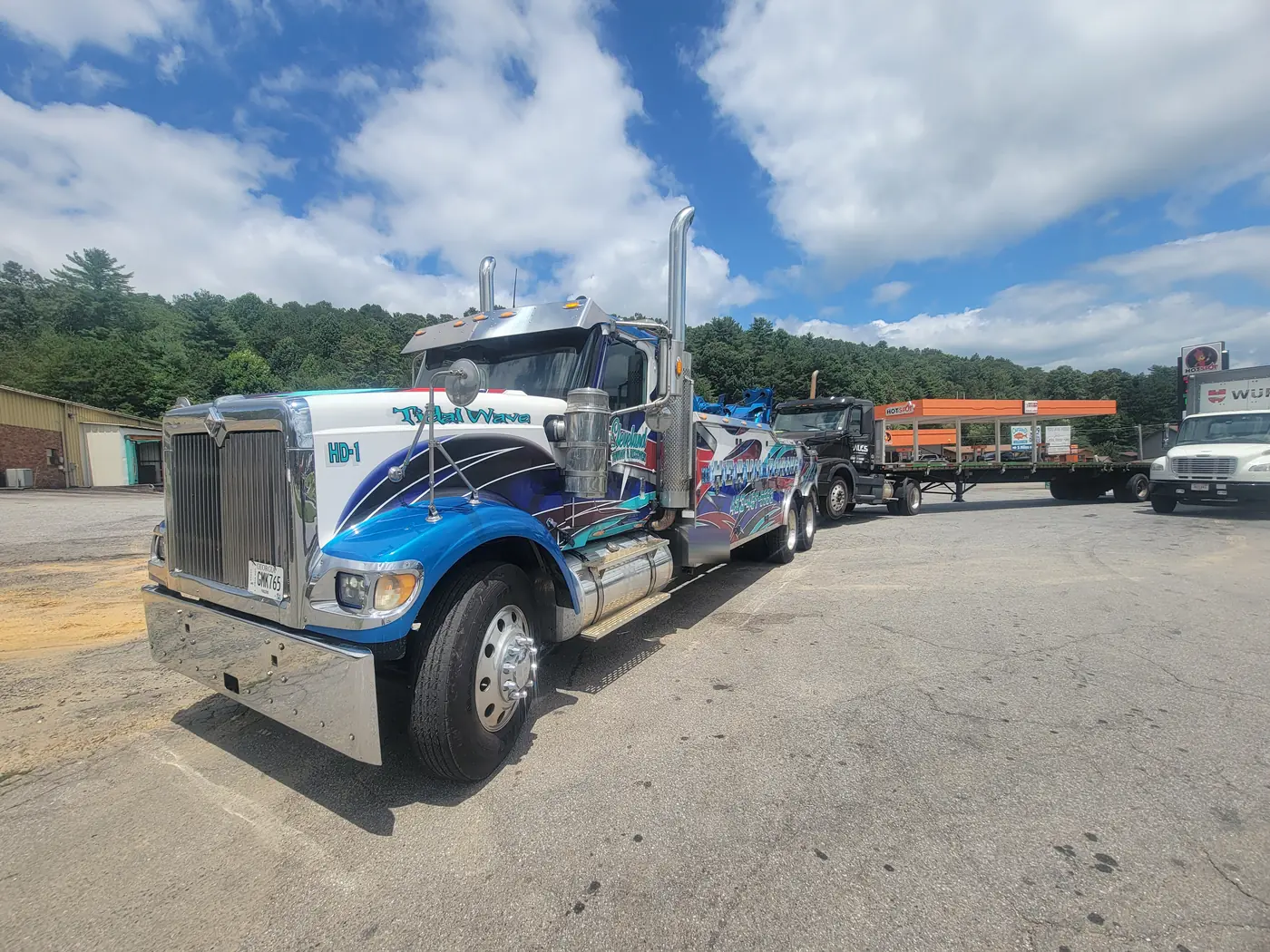A semi tractor and its flatbed trailer hooked to the heavy wrecker at a fuel stop