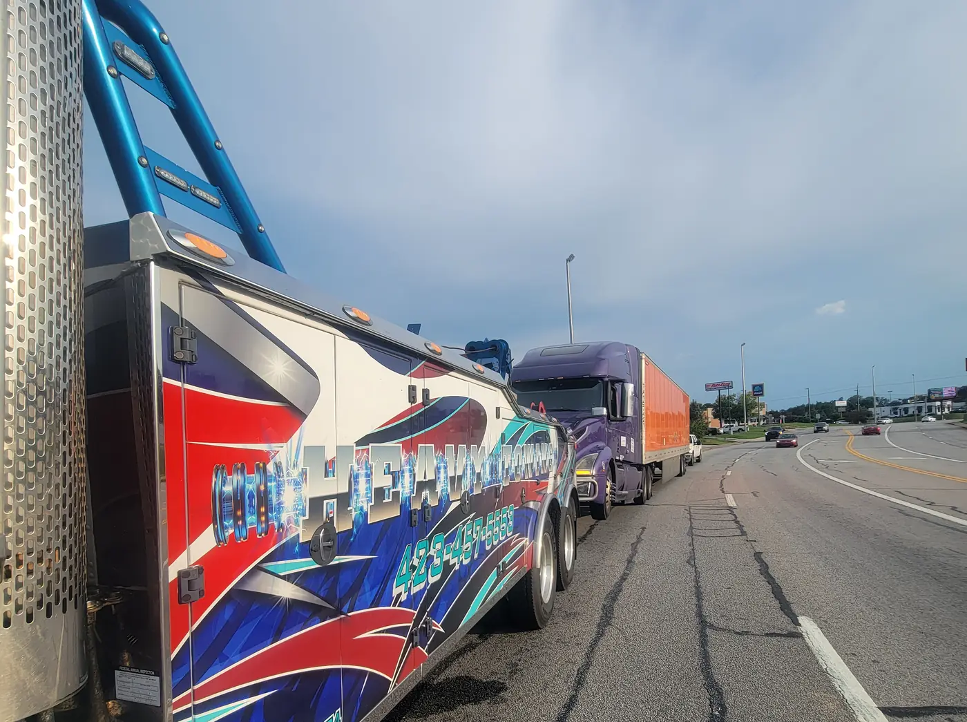 The wrecker’s boom rigged to a tractor-trailer stopped on the shoulder