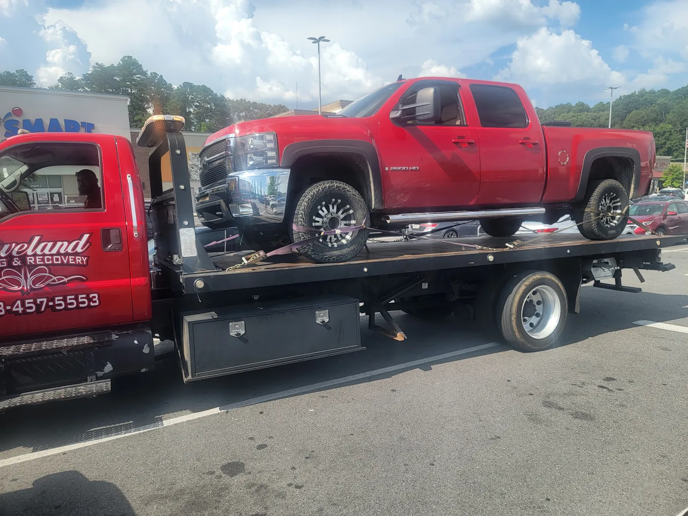 Cleveland Towing & Recovery’s red rollback with a pickup loaded and strapped down on the deck in a parking lot