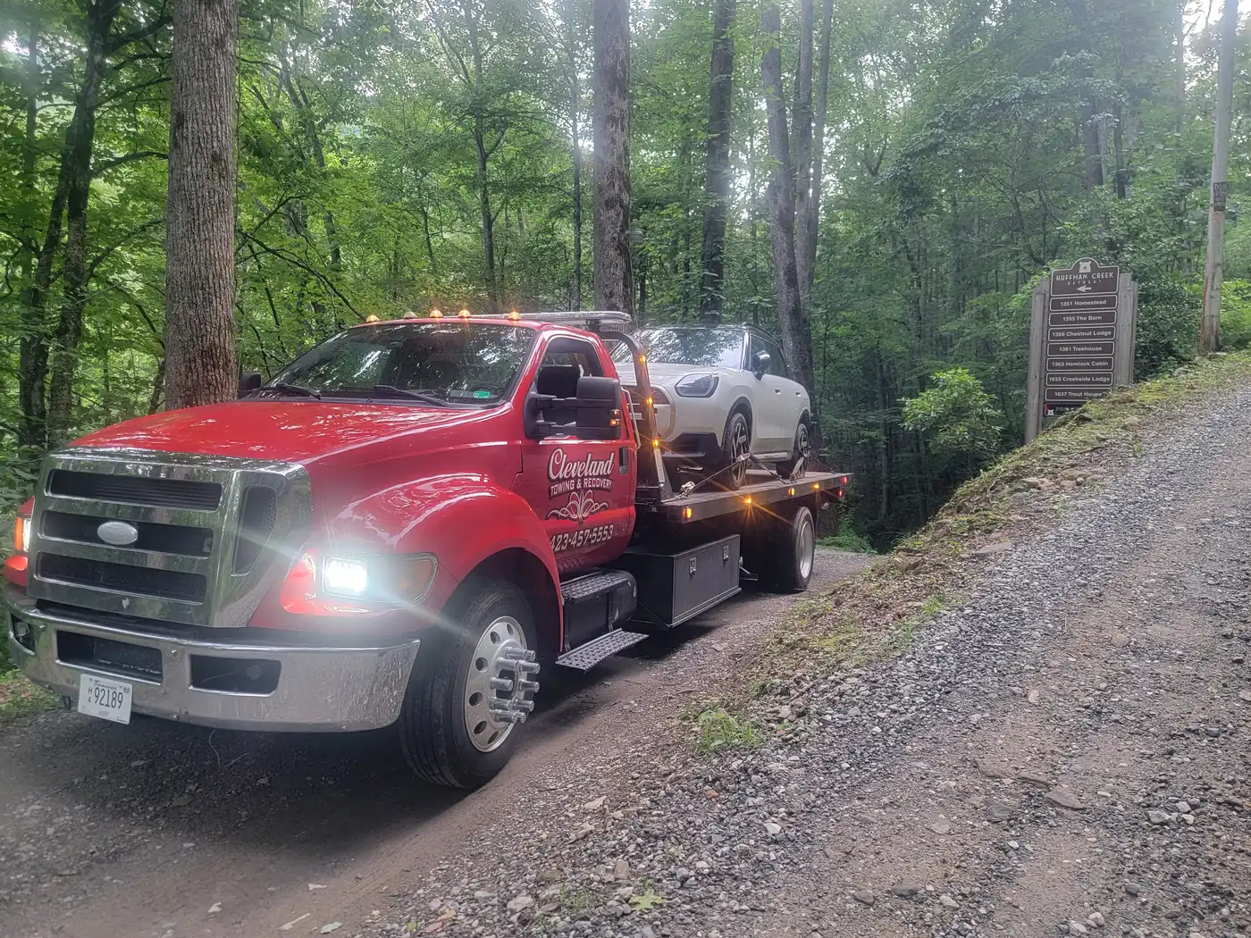 Our rollback with an SUV on the deck on a gravel back road, work lights on